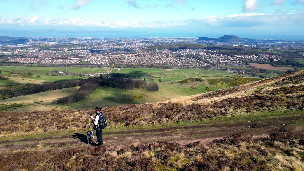 Jasper and his dog Jacks walking a hill path in the Pentlands, with Edinburgh below